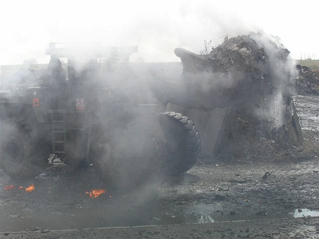 Hasii a vojáci tkou technikou rozebírají hromady hoícího odpadu.