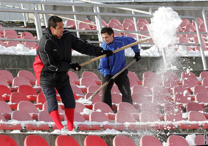 Fotbalisté 1. FC Brno uklízí sníh ze sedaek stadionu na Srbské