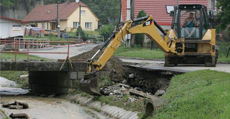 Bagrista opravuje podemletý beh silnice u Hluzovského potoka v ernotín. V této obci blízko Hranic nalezli osmou ob záplav (25. ervna 2009)