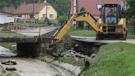 Bagrista opravuje podemletý beh silnice u Hluzovského potoka v ernotín. V této obci blízko Hranic nalezli osmou ob záplav (25. ervna 2009)