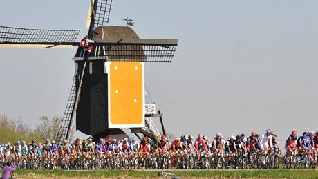 Cyklisté na trati závodu Amstel Gold race míjejí vtrný mlýn. 