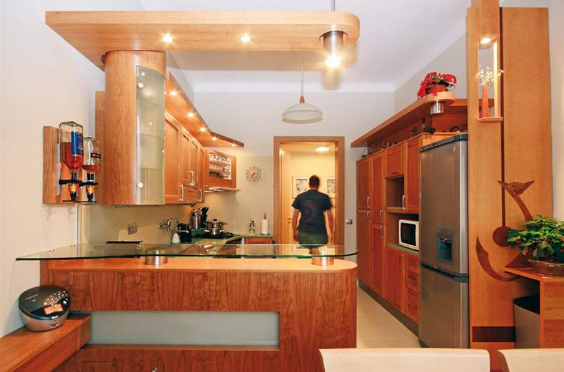 Kuchyská linka s ímsami, prosvtleným barem a dekorativní stnou s koií intarzií, která kryje bok chladniky