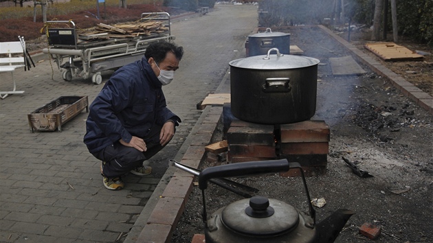 Japonec vaí jídlo nedaleko nemocnice ve mst Onagava, které zdevastovalo tsunami (25. bezna 2011)