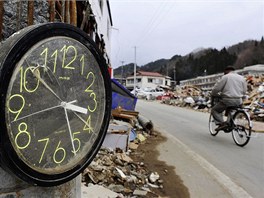 Mu na kole projd kolem hodin zastavench ped mscem pi tsunami v japonskm mst Miyako. (11. dubna 2011)