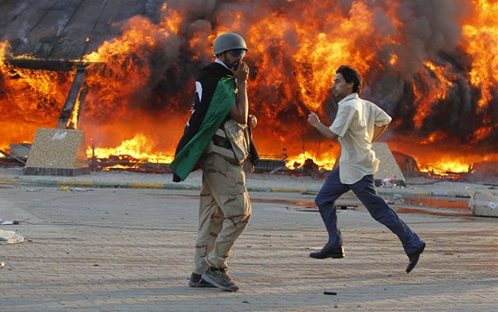Povstalec kráí kolem hoícího stanu v rezidenci Muammara Kaddáfího. (23. srpna 2011)