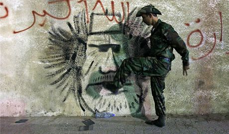 Libyjský voják Pechodné národní rady kope do zdi, na které je hanliv vyobrazen Muammar Kaddáfí. (20. íjna 2011)