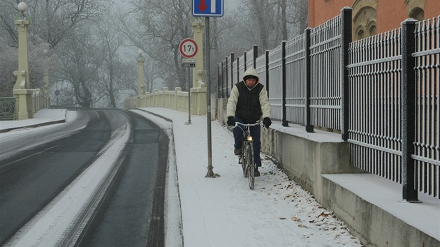Cyklista na zasneném chodníku u Kalikovského mlýna v Plzni.