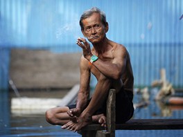 Postarí mu si uívá cigaretu ped svým vytopeným domem v bangkockém slumu....