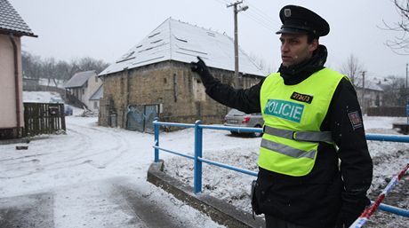 Policista hlídkuje u usedlosti s tajným skladem zbraní (vlevo vzadu).