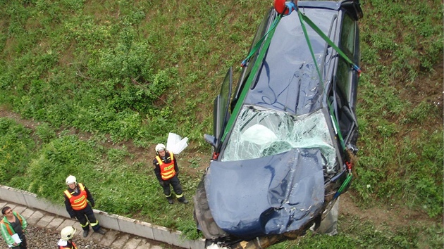 Jeáb zvedá havarované auto z kolejit.