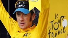 Cyklista Bradley Wiggins ve lutém dresu na pódiu mává fanoukm.