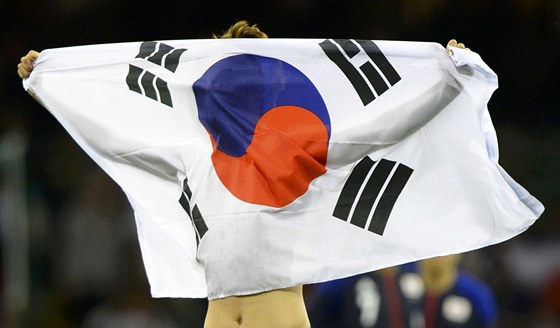 Korejský fotbalista slaví s vlajkou bronzové medaile z olympijských her. Jeho
