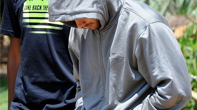 Policisté odvádějí atleta Oscara Pistoriuse (v kapuci) z policejní stanice v Pretorii v JAR. (14. února 2013)