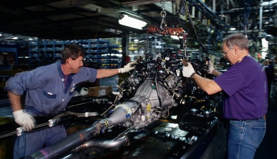 Dlníci instalují motor do fordu v automobilce Ford Motor Company. Ilustraní