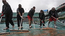 VODU PRY! Dobrovolníci odklízejí vodu z plachet na kurtech Rolanda Garrose.