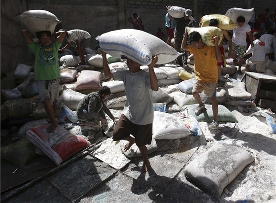Peiví obyvatelé Filipín odnáejí pytle s rýí ze znieného skladit. 