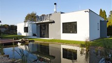 Střízlivá šedobílá architektura se zrcadlí v přírodním jezírku. Zapuštěná Střízlivá šedobílá architektura se zrcadlí v přírodním jezírku. Zapuštěná