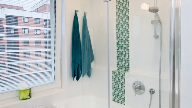 Koupelnu v bl barv oivuj svisl pruhy zelen mozaiky.