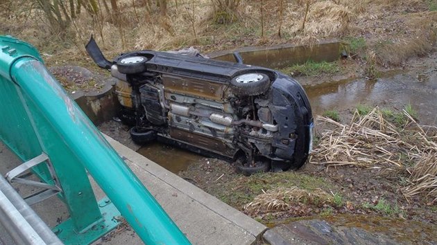 Automobil se dvma pasary skonil na boku v potoce pod mostkem (23. bezna 2014).