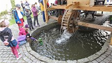 U mlýnského kola se z vody vynouje vodník.