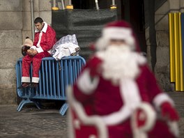 A man who performs for money wearing a Santa Claus outfit eats a sandwich as...