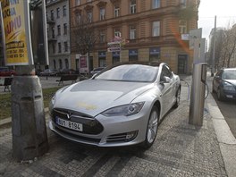 Elektromobil stojí při dobíjení na chodníku. Na silnici z druhé strany je...