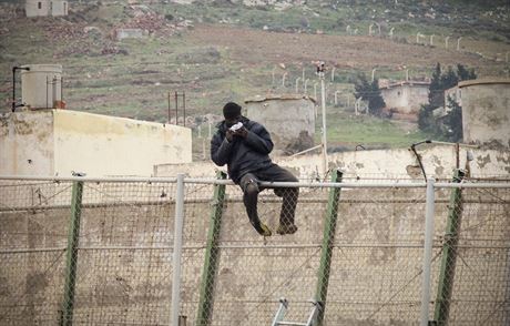 Africký uprchlík na plotu mezi Melillou a Marokem pojídá sendvi, který mu...