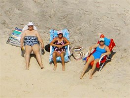 File photo of beach goers sunbathing behind a wall of hay bales,...