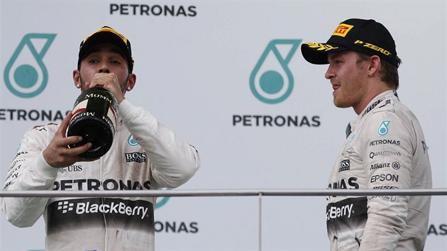 Lewis Hamilton si dv douek ampaskho, tmov kolega Nico Rosberg ho se zjmem pozoruje. Oba borci z Mercedesu se v Malajsii museli sklonit ped Sebastianem Vettelem.