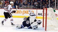 Branká Ondej Pavelec z  Winnipegu elí nájezdu chicagského Patricka Sharpa.