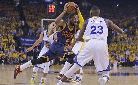 Kyrie Irving (v tmavém) z Clevelandu najídí mezi  Draymonda Greena (23) a...