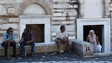 Lidé v Aténách sedící ped ortodoxním kostelem ozdobeným eckými vlajkami.