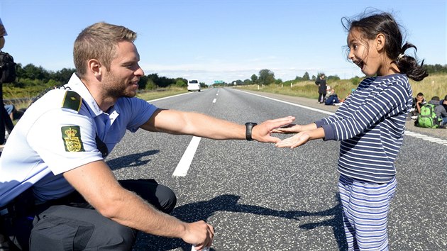 Dnsk policista si hraje s jednou z malch uprchlic na silnici smrem do vdska. (9. z 2015)