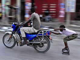JÍZDA. Chlapec na kolekových bruslích si cestu ulicemi Port-au-Prince na Haiti...
