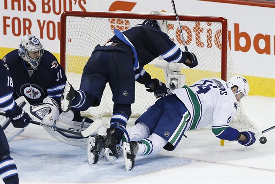 Branká Ondej Pavelec sleduje, jak si jeho spoluhrá z Winnipegu Adam Pardy...