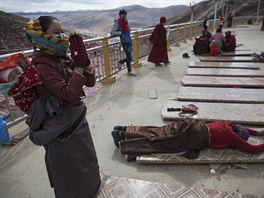 Ethnic Tibetan woman, carrying her baby on the back, prays at a monastery above...