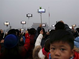 SMOG V PEKINGU. Lidé si natáejí ceremoniál vyvování vlajky uprosted hustého...