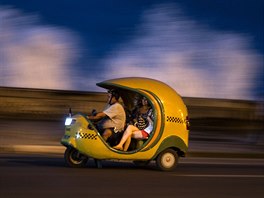 COCO TAXI. Turisté cestují v takzvaném Coco taxi po havanském nábeí Malecón....