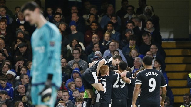 Fotbalist Watfordu se raduj ze vstelenho glu na stadionu Chelsea, zatmco domc brank Thibaut Courtois zklaman hled k zemi.