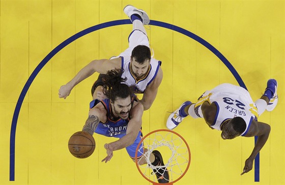 Steven Adams (v modrém) z Oklahoma City zakonuje na ko Golden State, brání ho...