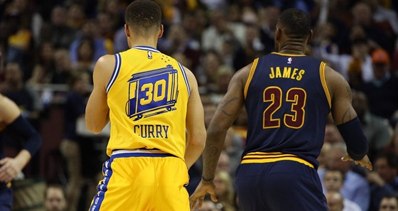 Stephen Curry (vlevo) a LeBron James sledují hru.