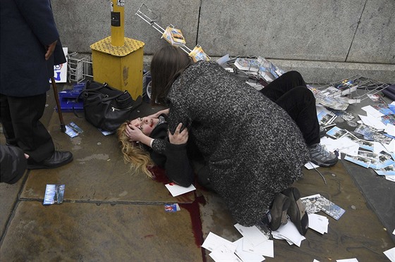 Lidé pomáhají en, kterou zranil útoník nedaleko budovy britského parlamentu....