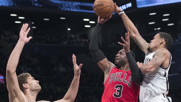 Dwyane Wade z Chicaga stl pes Brooka Lopeze z Brooklynu, m se mu pokou srazit K. J. McDaniels.