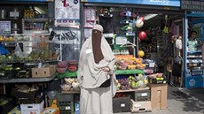 Muslimka zahalená v nikábu pózuje před pouličním krámkem v Londýně. Muslimka zahalená v nikábu pózuje před pouličním krámkem v Londýně.