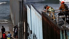Migranti pihlíejí dlníkm, kteí osazují hraniní zátaras u Tijuany ostnatým...