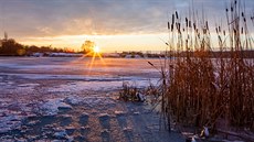Slunce zapadající nad stále jet zamrzlým jezerem Chomoutov na Olomoucku. (4....