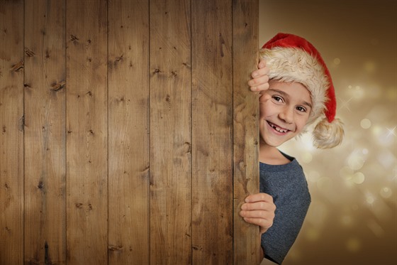 Lachender Junge mit Weihnachtsmtze hinter Holzwand