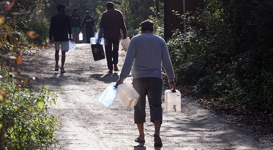 Migranti v uprchlickém táboe Vujak v Bosn nesou kanystry s vodou. Úady jim...