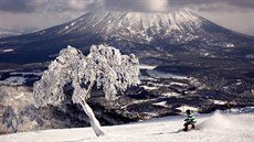 SJEZDOVÁNÍ U SOPKY. Snowboardista brázdí sjezdovku v lyžařském areálu na... SJEZDOVÁNÍ U SOPKY. Snowboardista brázdí sjezdovku v lyžařském areálu na...