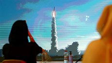 Lidé sledují na velkoploné obrazovce v Dubaji start rakety H-IIA, která...